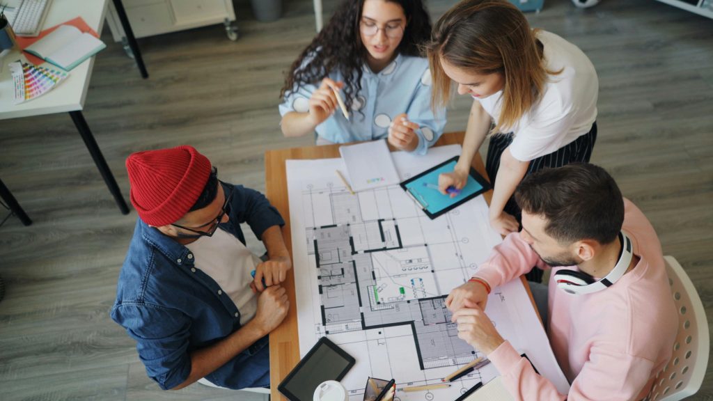 Diverse group of young adults working together on architectural plans in a modern office.